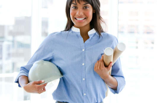 Smiling,Female,Architect,Holding,A,Hardhat,And,Blueprints,Standing,In